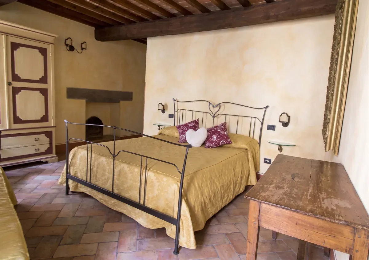 Camera Porta Romana: letto matrimoniale davanti al camino in pietra, armadio dipinto e travi a vista